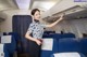 A woman in a blue and white shirt is standing in an airplane.