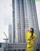 A woman in a yellow dress standing in front of a tall building.