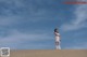 A woman in a white dress standing on top of a sand dune.