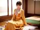 A woman in a yellow kimono sitting on a bed.