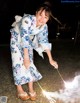 A woman in a blue and white kimono holding a sparkler.